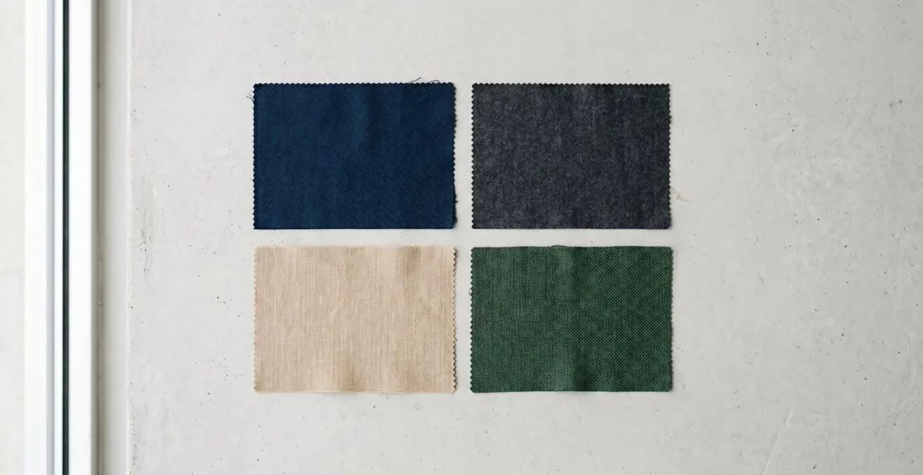 Composition minimaliste montrant des échantillons de tissus de costumes dans des nuances alternatives au noir : bleu nuit, gris anthracite, beige sable