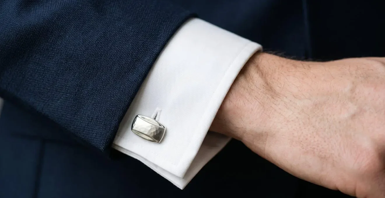 Gros plan macro sur les détails d'un costume formel : manchette de chemise blanche dépassant de la veste, bouton de manchette élégant en argent
