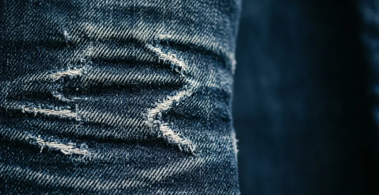 Gros plan détaillé d'un jean brut indigo avec patine naturelle montrant les plis et décolorations caractéristiques