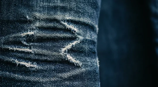 Gros plan détaillé d'un jean brut indigo avec patine naturelle montrant les plis et décolorations caractéristiques